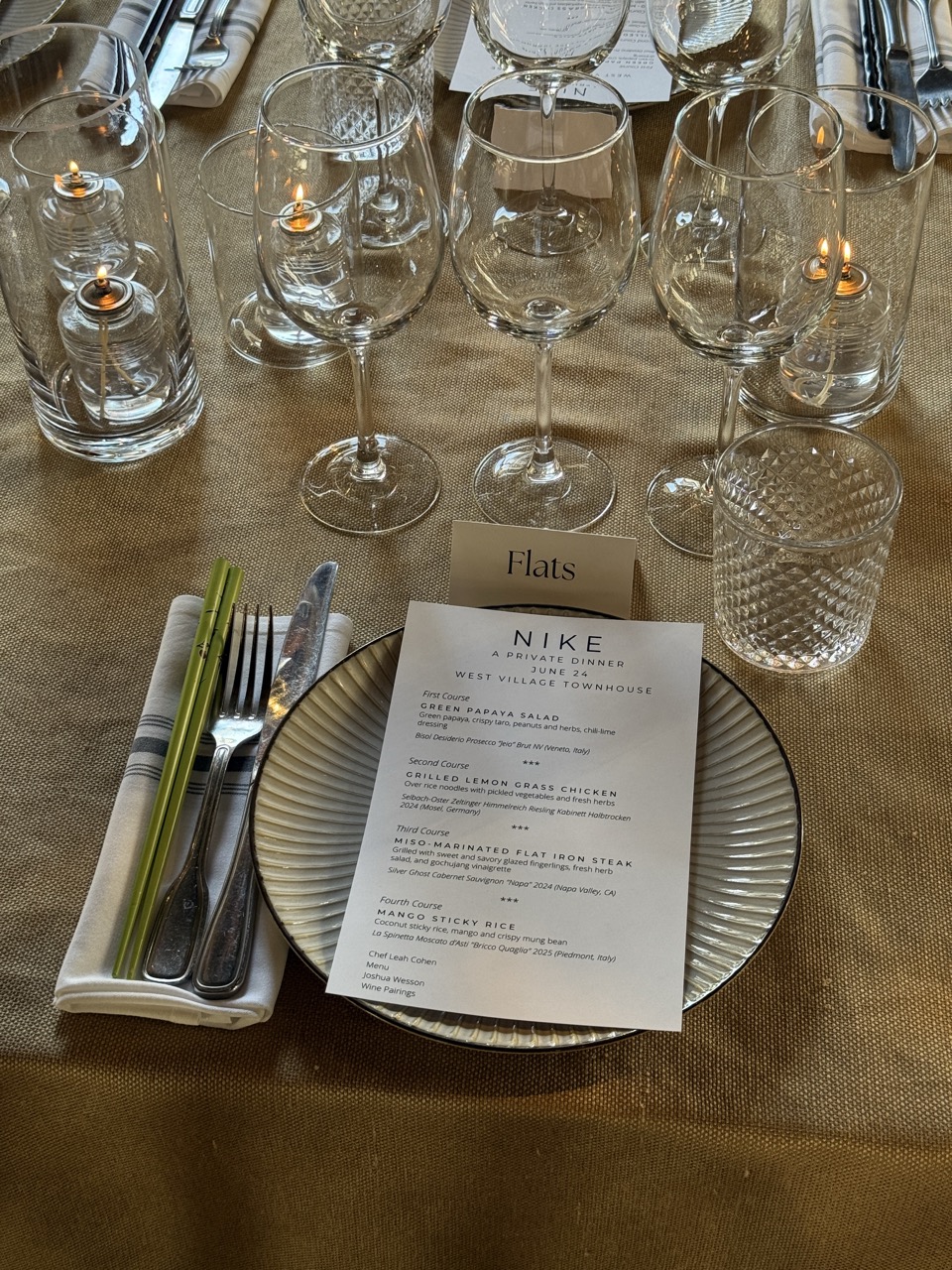 Nike private dinner place setting with custom menu, wine glasses, candles, and tableware.